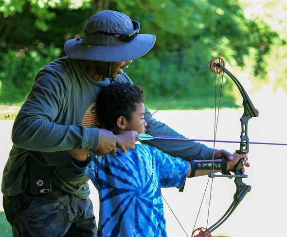 Scout leader coaching a young Scout on the archery range